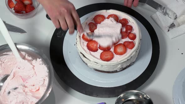 Front Shot of a Baker Using an Icing Spatula to Carefully Touch Up Sides of Cream Covered Cake