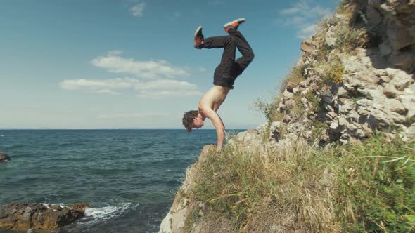 Young caucasian male does an extended handstand on a cliffside overlooking the ocean.