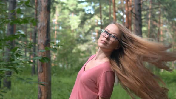 Girl with long, blonde, swaying hair turning around outdoor in summer park.