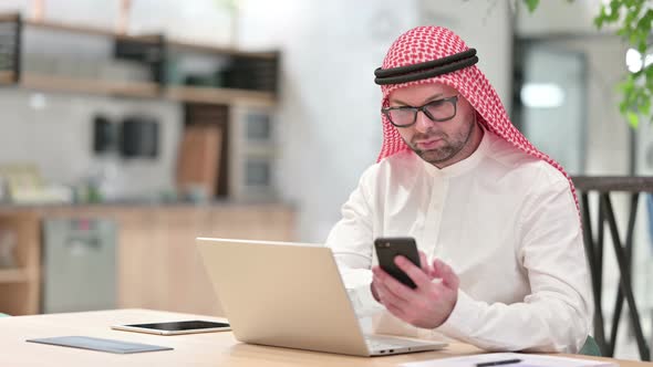 Professional Young Arab Businessman Using Smartphone and Laptop in Office 