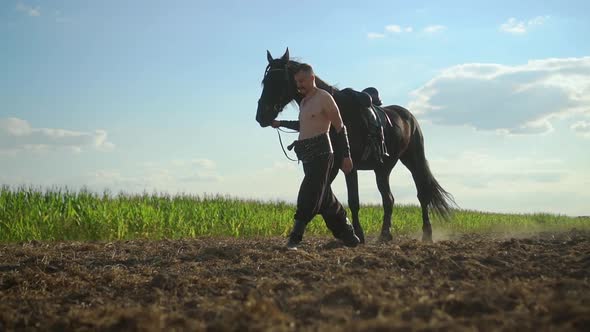 Man Walks with a Horse in the Field