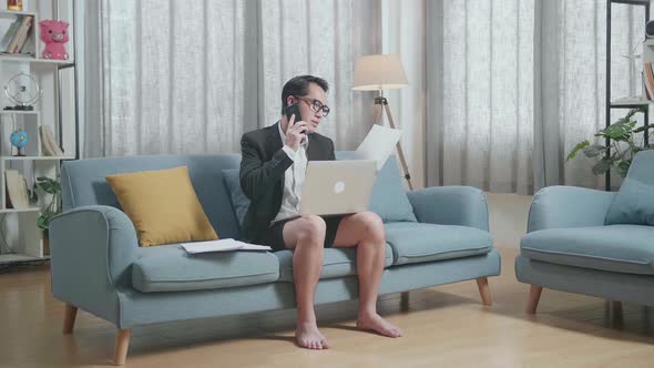 Businessman In Jacket And Shorts Holding A Paper And Talking On Phone While Working With A Laptop