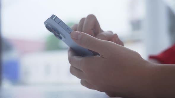 Closeup of Person's Hands Typing on Text on New Phone Against Background of Bright Street with