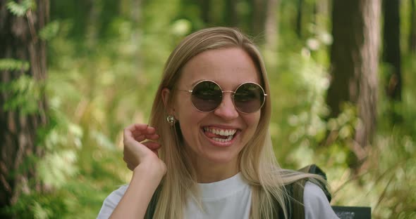 A Young Female Traveler in Sunglasses Looks Directly at the Camera and Smiles Flirting, a Traveler