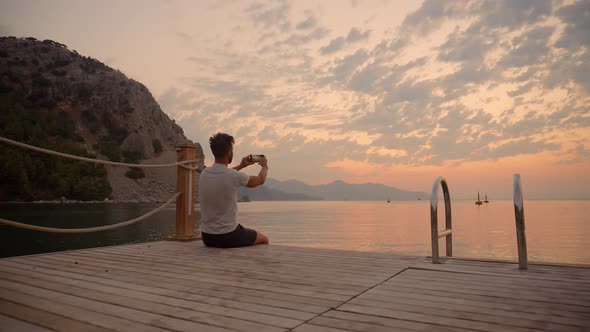 Selfie At Sunset Over Sea In Vacation Holiday. Man Sitting On Embankment And Taking Selfie On Sunset