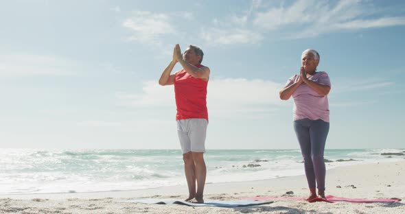 Relaxed hispanic senior couple practicing yoga on mats on beach