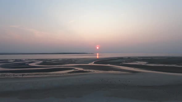 Aerial descending, drone shot of water canals patterns on a beach, towards sunset