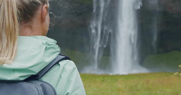 Closeup of Female Traveler Back with Backpack Loking to Beautiful Seljalandsfoss Waterfall Iceland