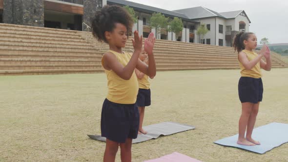 Video of focused diverse girls practicing yoga on mats in front of school