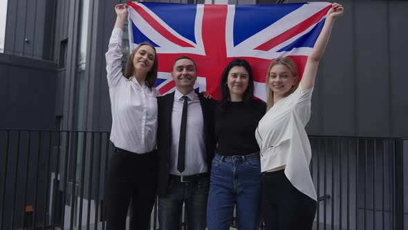 Four Confident British Business People Raising National Flag in Slow Motion Looking at Camera