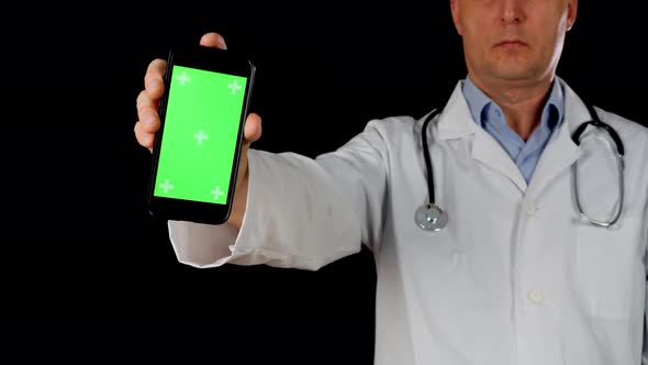 Doctor Holding Mobile Phone with Green Chromakey Screen on Black Background. Doctor in Medical Gown