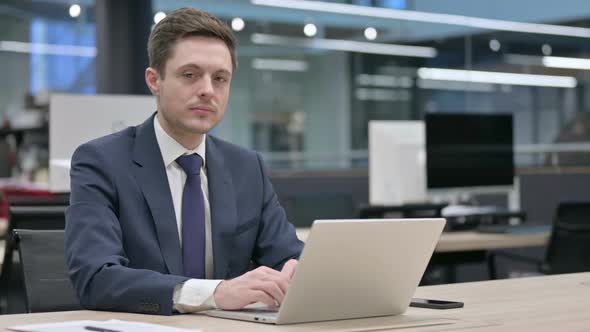 Businessman Smiling at Camera While Using Laptop in Office