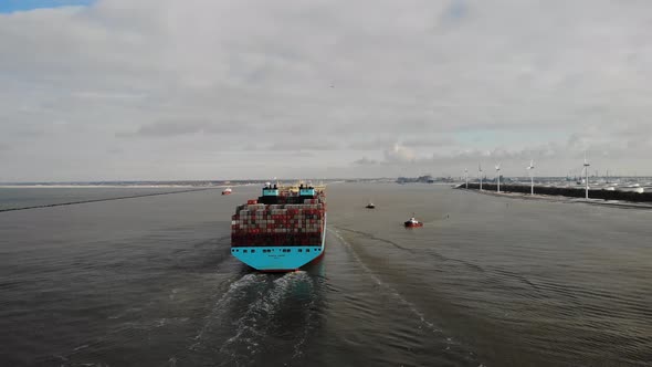 Giant container ship with two engines navigating slowly into the port of Rotterdam while two small t