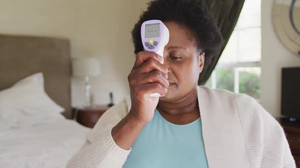 African american senior woman measuring her temperature while sitting on the bed at home