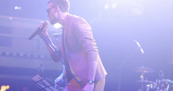 Attractive Young Male Singer in Glasses Performing with Band at Live Music Event