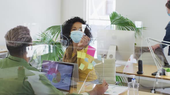 Woman wearing face mask writing on glass board on her desk at office