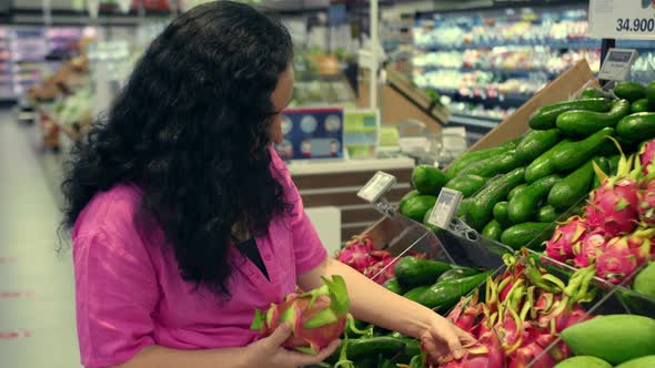 Pretty Young Woman in a Pink Suit is Making Purchases in Supermarket Choosing Products at