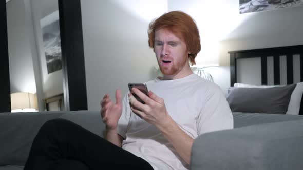 Redhead Man Upset for Loss While Using Smartphone