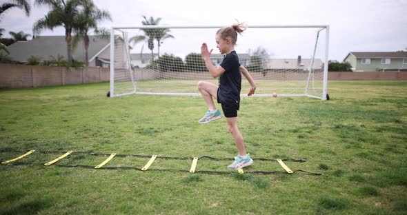 A young girl warms up for soccer practice on a speed ladder as she does high knees.