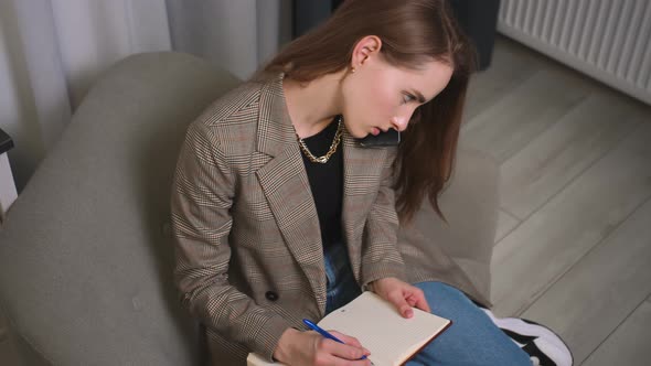 Pretty Caucasian Woman Talking on Phone Writing Notes in Notepad