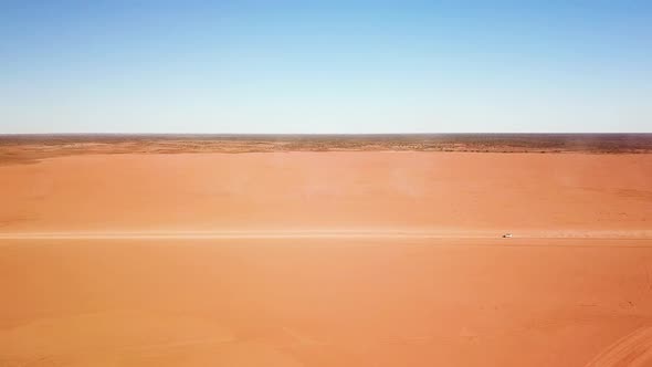 Stationary side-on aerial shot of car speeding across expansive, desolate, flat dirt area leaving la