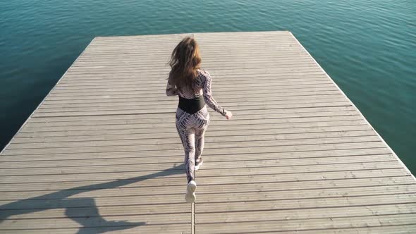 girl athlete with a beautiful figure runs on the pier of the lake. Slow motion. Top view