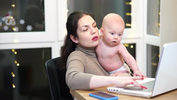 Young Woman with Toddler in Arms Typing on Laptop Remote Work with a Baby at Home