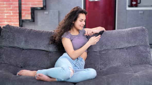 Happy Enthusiastic Young Casual Barefoot Woman Typing Message Using Smartphone at Home