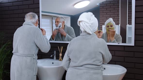 Senior Grandmother Applying Facial Mask and Grandfather Shaving with Manual Razor Blade at Bathroom