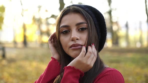 Portrait of Beautiful Browneyed Brunette in a Cap Looking Into Camera in Park