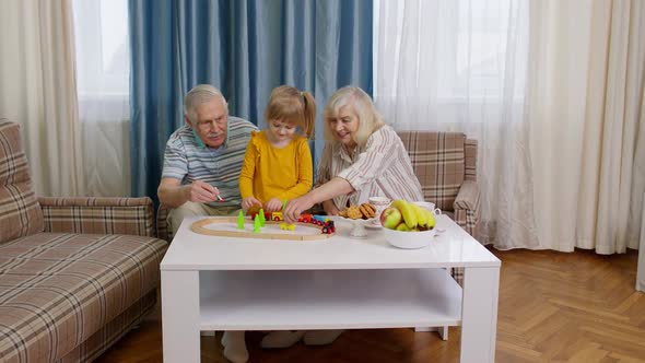 Senior Grandparents with Child Kid Granddaughter Playing Game Riding Toy Train on Railway at Home