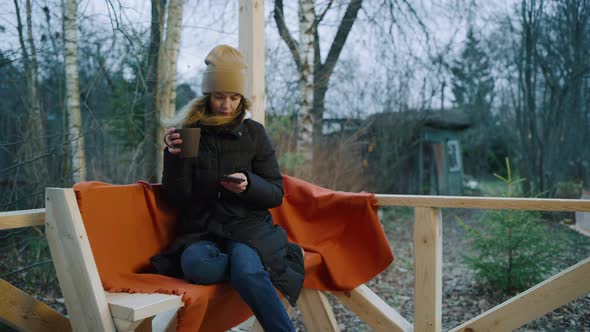 A Woman Sits on a Bench in the Courtyard and Types Text Into a Smartphone