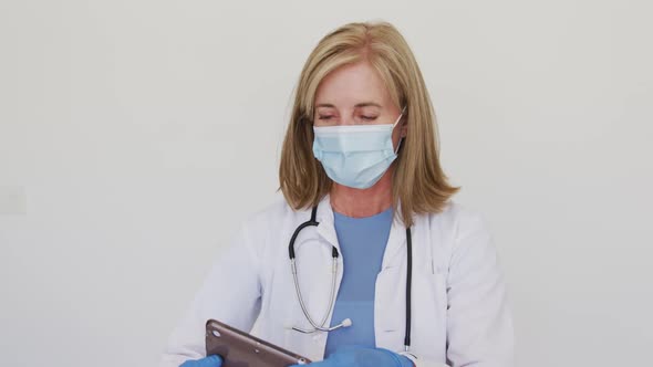 Portrait of caucasian senior female doctor wearing surgical gloves and face mask using tablet comput