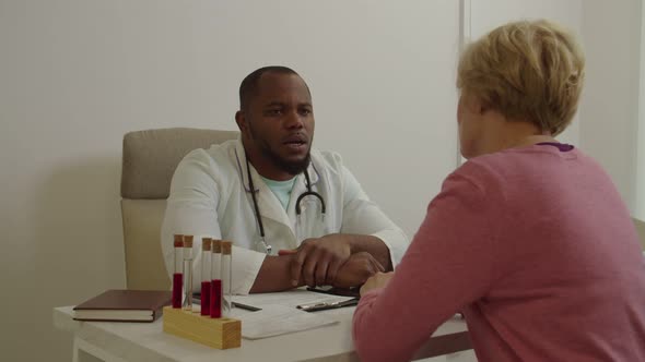 Happy Positive Middle Aged Woman Thanking Black Male Physician for Recovery and Help at Hospital