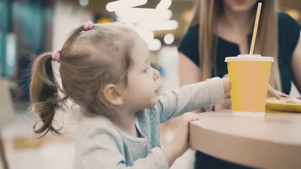 Mom Feeds a Little Daughter with a Fork They Sit in a Cafe