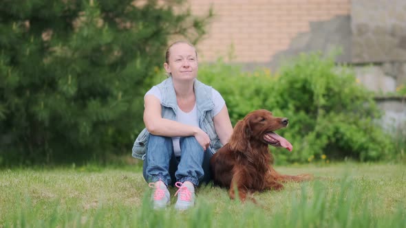 woman with dog sitting on green lawn near country house