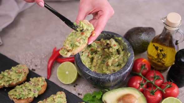 Woman Making Bruschetta with Freshly Made Guacamole Sauce at Domestic Kitchen