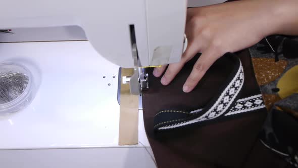 Hands and fingers pushing outside edge of brown cloth on handbag through Sewing machine for stitchin