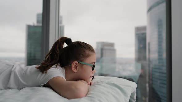 Cute Teenage Girl Relaxes on a Comfortable Bed Looking at the City From a Height