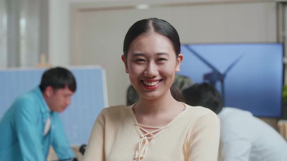 Smiling Asian Woman Engineer Crossing Her Arms To Camera While Her Colleagues Are Discussing Work