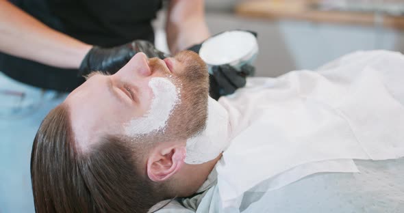 Closeup Hands of Female Barber Who Applies with Brush Shaving Cream on Young Bearded Man's Face and