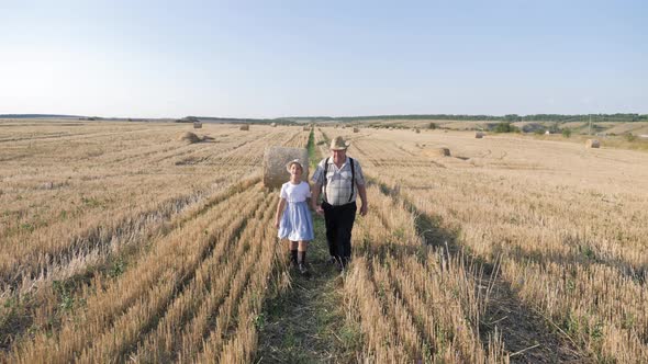 Grandfather and Granddaughter Walking Across the Field with Haystacks