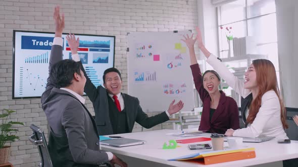 Asian business team celebrating success together in boardroom.