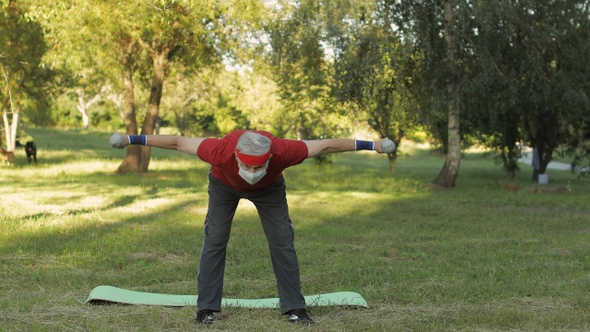 Senior Grandfather Making Fitness Exercises with Dumbbells During Coronavirus Pandemic Alone in Park