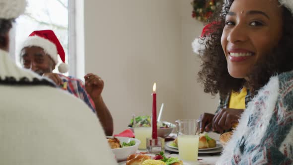 Portrait of smiling african american woman wearing santa hat celebrating holiday meal with family