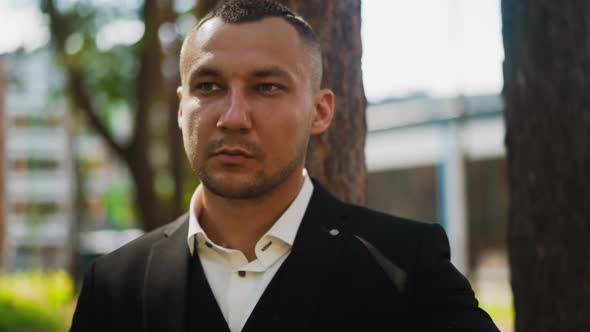 Man in Classic Black Suit Looks Aside Standing in City Park