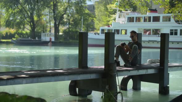 Men Enjoying His Free Time Playing with His Smartphone on the Pier