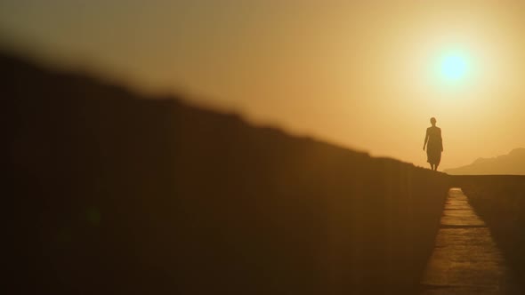 Woman in a Red Dress and a Straw Hat Walks Along the Edge Front of a Cliff By the Sea Alone at