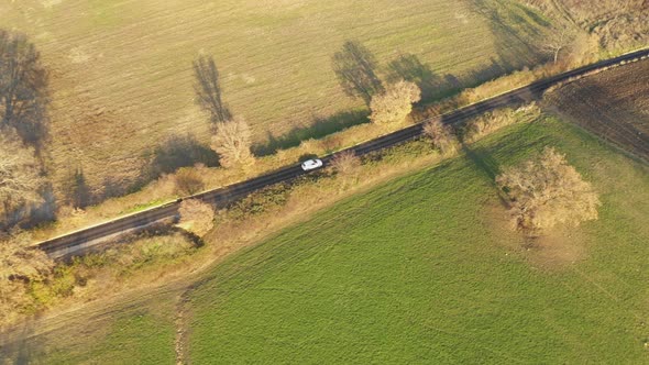 Aerial view of a white car driving through orange autumn countryside at sunse