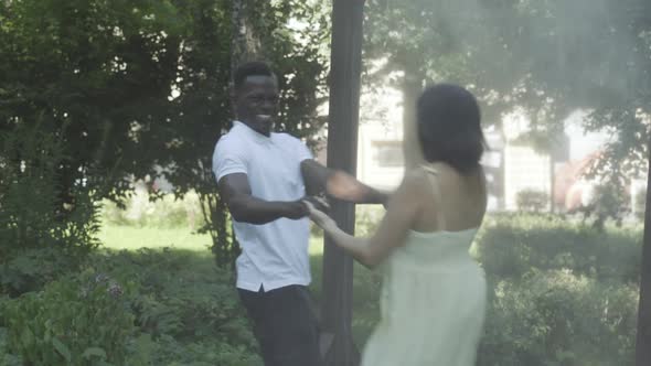 Happy Joyful Interracial Couple Spinning in Sunlight Outdoors and Smiling. Cheerful African American